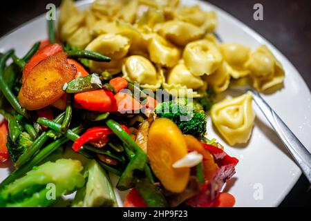 Assiette de légumes blanche avec mélange de carottes, de légumes rouges au brocoli et de pâtes de remplissage au fromage tortellini à la sauce sur le backgrou de table Banque D'Images