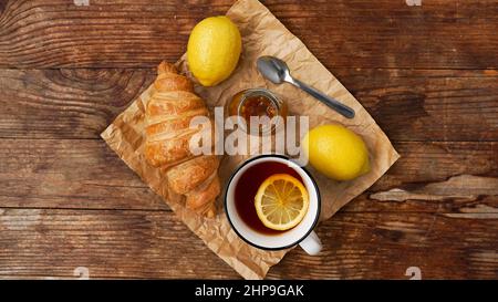 Thé au citron, confiture faite maison, croissant sur table en bois. Concept petit déjeuner. Vue de dessus Banque D'Images