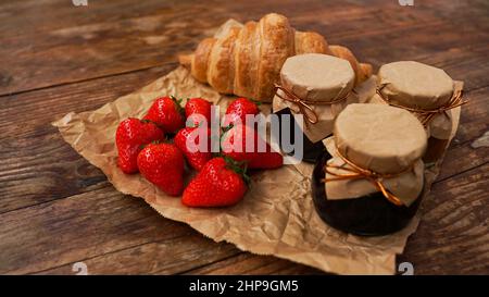 Confiture de fraises dans le pot en verre avec baies fraîches et croissant sur fond de bois. Fait maison. Ingrédients pour faire du pain grillé pour un délicieux petit déjeuner Banque D'Images