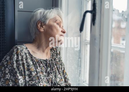 Photo latérale d'une grand-mère européenne âgée tout seule pendant la journée des grands-parents et regardant doucement par la fenêtre. Photo de haute qualité Banque D'Images