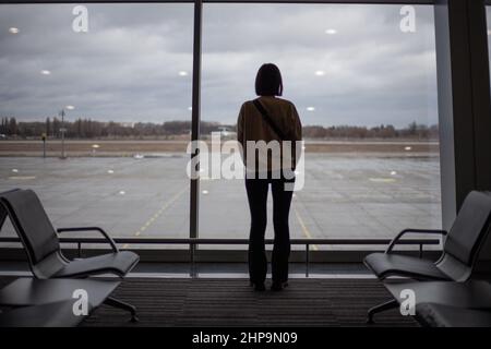 Une fille se tient devant une grande fenêtre en vitraux à l'intérieur de l'aéroport Banque D'Images