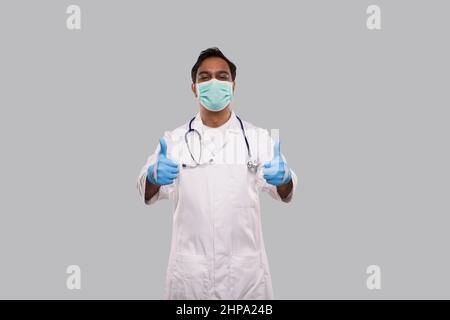 Médecin montrant Thumb Up les deux mains en portant un masque médical et des gants. Indian Man Doctor Isolated Banque D'Images