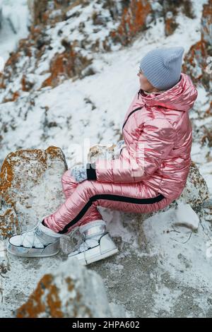 La femme est assise dans la colline. Le voyageur marche en haut de la montagne. Belle fille est vêtue d'une élégante veste en duvet rose. Explorer a l'air afar, sur un être Banque D'Images