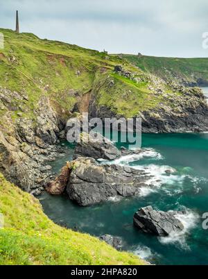 Mer Atlantique bleu et vert calme en été, cheminée de mine d'étain et bâtiments miniers ruinés sur les falaises, soleil sur les rochers déchiquetés sous les falaises Banque D'Images