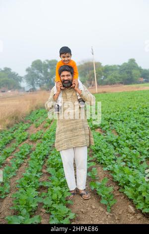 Heureux fils indiens assis sur l'épaule de père ayant le plaisir dans le domaine agricole, passer du temps libre ensemble dans la ferme, enfant de garçon profiter de l'enfance avec l'homme o Banque D'Images