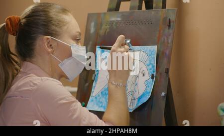 Une artiste apprend à peindre avec un aérographe avec du colorant acrylique, du papier et du chevalet. Intérieur. Concept art moderne, aérographe, aérographie, dessin pulvérisation image créer pulvérisateur dessin graffiti aérosol spray Banque D'Images
