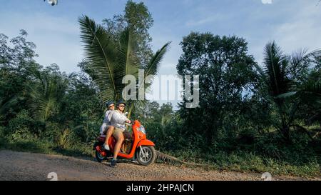 J'adore un couple sur une moto rouge vêque de vêtements blancs pour faire un voyage sur la route de la forêt. Deux touristes caucasiens, homme, conduisent en scooter. Location de moto, casque de sécurité, lunettes de soleil. Asie Thaïlande Ride tourisme. Banque D'Images