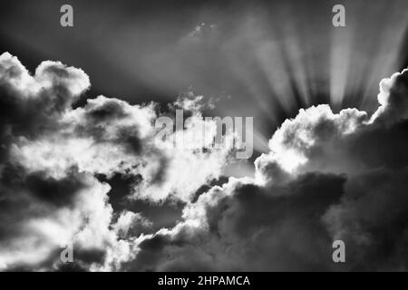 Les niveaux de gris contrastent le ciel spectaculaire avec les nuages orageux pénétrés par les rayons du soleil levant comme doublure argentée. Banque D'Images