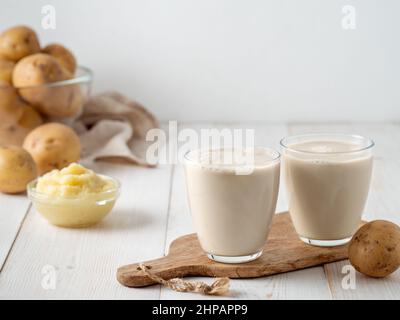 Lait de pomme de terre en verres sur fond blanc en bois. Verser le lait végétalien dans le verre, avec la purée de pommes de terre et les tubercules de pommes de terre sur le fond. Copier l'espace. Lait de pomme de terre fait maison à base de pommes de terre bouillies Banque D'Images