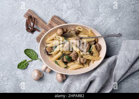 Vue de dessus de savoureux penne de pâtes et champignons dans un bol avec feuilles d'épinards et sauce à la crème sur fond de béton gris Banque D'Images