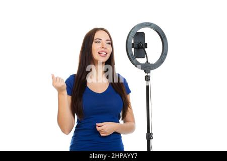 La belle fille blogger communique avec les abonnés de son canal en utilisant un smartphone et un anneau lumineux. Banque D'Images