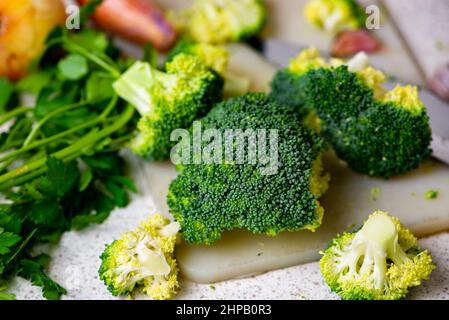 Fleurons de brocoli crus, persil et oignon sur le plan de cuisine sur la table, ingrédients pour la soupe, gros plan. Préparation de légumes. Banque D'Images