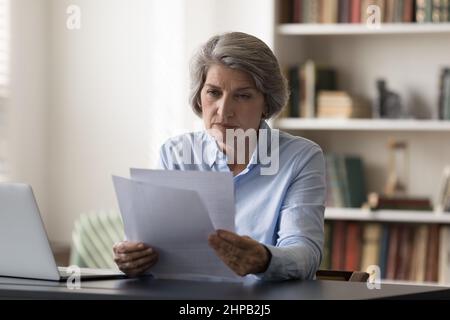 Femme d'affaires d'âge moyen concentrée qui fait de la paperasserie financière. Banque D'Images