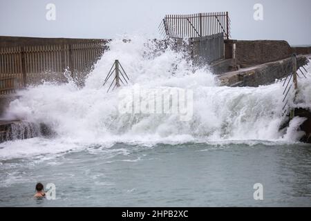 Portreath,Cornwall,20th février 2022, les vagues se écraseront sur le mur du port alors qu'une dame prend une baignade tôt le matin. Les mers commencent à se calmer après la tempête qu'Eunice a frappé Portreath, en Cornouailles. La prévision est pour des vents plus forts cet après-midi et un avertissement jaune a été émis par le met Office.Credit: Keith Larby/Alay Live News Banque D'Images