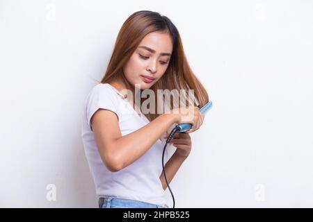 jeune asiatique belle femme heureuse lissant les cheveux avec un lisseur sur fond blanc Banque D'Images