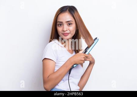 jeune asiatique belle femme heureuse lissant les cheveux avec un lisseur sur fond blanc Banque D'Images