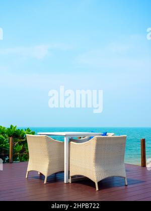 Mobilier moderne en rotin blanc vide, table de jardin extérieure tissée avec table et trois chaises sur la terrasse sur la plage avec vue sur la mer et ciel bleu Banque D'Images