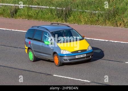 2002 multicolore, personnalisé, personnalisé Ford Galaxy LX TDI manuelle à 6 vitesses, habillage voiture, vinyle sur graphiques sur car wrapping coloré avec capot jaune et roues de différentes couleurs ; voyager sur l'autoroute M6, Royaume-Uni Banque D'Images