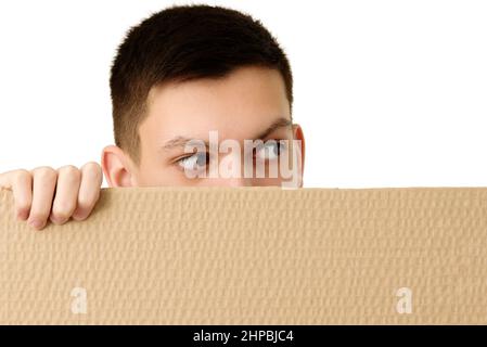 Adolescent avec des yeux bien piqués dehors de derrière la bannière en carton brun vierge, isolé sur fond blanc. Gros plan. Copier l'espace Banque D'Images