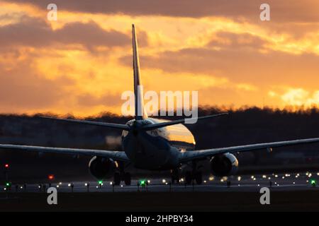 Avion prêt pour le décollage à l'aéroport de Stuttgart, dans un ciel de coucher de soleil doré avec quelques nuages, partiellement brouillé par la chaleur des moteurs à réaction Banque D'Images