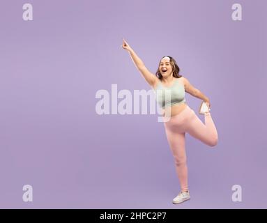 Bonne surprise excitée plus grande taille européenne jeune femme dans sportswear faisant l'exercice de jambe Banque D'Images