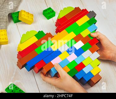 Un enfant tient un cœur en briques lego entre ses mains. Cadeau d'un enfant. Le concept de l'amour, de la famille et d'un don aux parents Banque D'Images