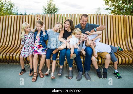 Portrait de famille ridicule et drôle sur banc en bois à l'extérieur. Banque D'Images