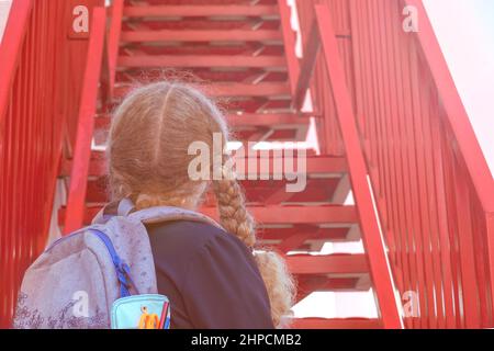 Une écolière regardant les escaliers...Concept école jours, date de début, étape suivante, échelle de carrière, le début de la voie. Fille dans un uniforme avec un bac Banque D'Images