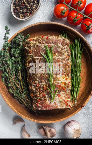 Porchetta italienne crue assaisonnée d'herbes, rouleau de viande de porc. Arrière-plan blanc. Vue de dessus Banque D'Images