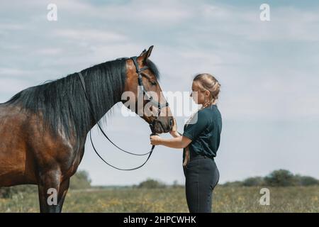 Jeune femme debout à côté du cheval sur le terrain et touchant le museau de cheval avec la main. Banque D'Images