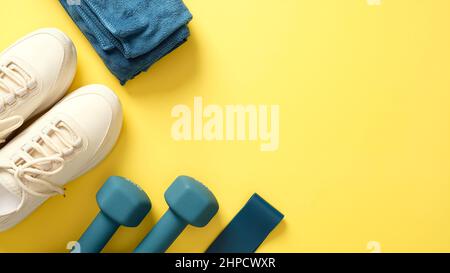 Équipement de fitness pour les entraînements sur fond jaune, vue de dessus. Flat Lay chaussures de sport féminines, serviette, haltères, ruban de fitness Banque D'Images