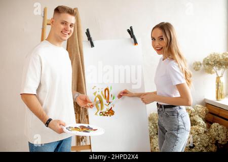 Couple souriant stand peindre sur toile en utilisant la palette d'aquarelle, des pinceaux près de l'échelle en bois et un bouquet de fleurs séchées. Banque D'Images