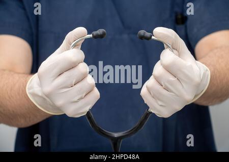 Médecin en uniforme médical tient, à la main avec un gant jetable, tube stéthoscope avec écouteur. Soins de santé, diagnostic d'un médecin professionnel. Banque D'Images