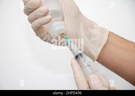 Main du médecin avec un gant jetable, en remplissant la seringue avec l'aiguille du flacon de médicament en plastique sur fond blanc. Soins de santé, traitement de la phy professionnelle Banque D'Images