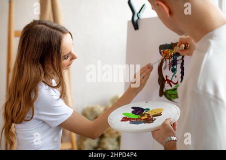 Jeune couple mignon stand peindre avec enthousiasme sur la toile en utilisant la palette d'aquarelle, les brosses près de l'échelle. Art thérapie. Banque D'Images