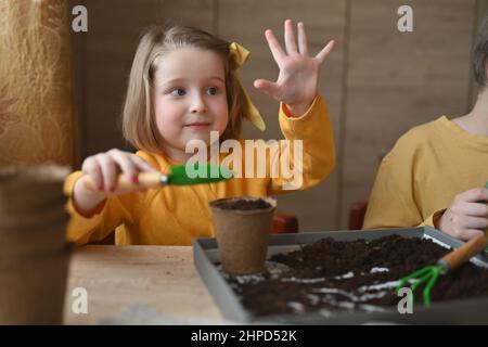 concept de jardinage. petite fille est engagée dans la plantation de semences pour les semis, versant la terre dans des pots pour les cultures. Banque D'Images