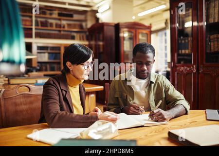 Portrait d'une femme mature professeur tutorat afro-américain étudiant en intérieur de bibliothèque classique à l'université Banque D'Images