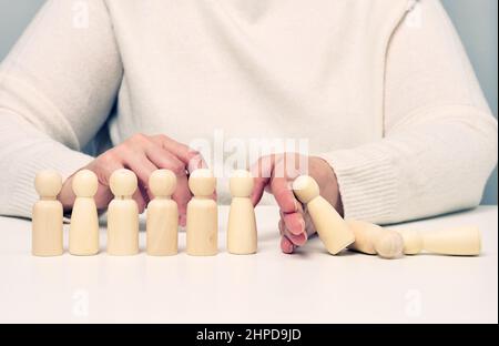 la main arrête la chute de figurines en bois d'hommes sur un fond blanc.Concept d'une personnalité forte et courageuse capable de résister à l'inégalité d Banque D'Images