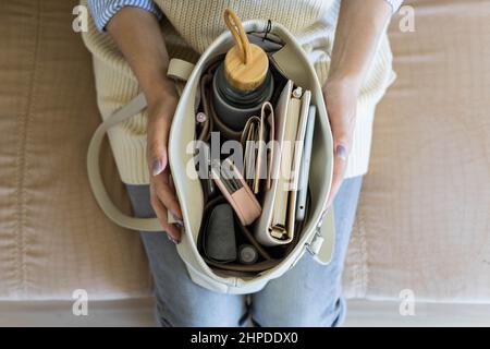 Vue du dessus gros plan femmes mains tenant un sac à main moderne plein d'accessoires personnels dans le rangement en feutre Banque D'Images