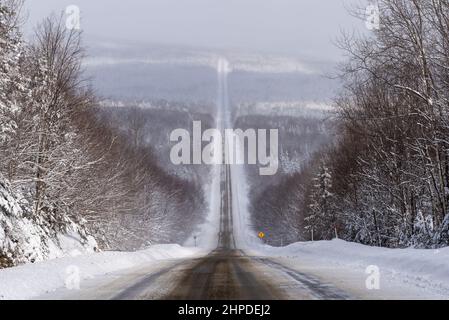 Route uebec 216, dans la région de Chaudière-Appalaches, en hiver avec une grande vue panoramique sur la forêt neigeuse bordant la route neigeuse partielle. Banque D'Images