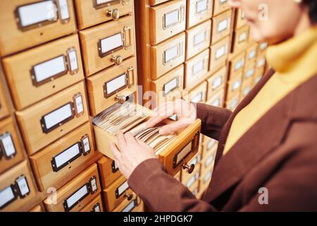 Gros plan d'une bibliothécaire féminine recherchant un livre dans l'armoire du catalogue de la bibliothèque, espace de copie Banque D'Images