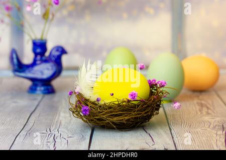 Composition festive de Pâques sur une table en bois gris avec un œuf de poulet jaune vif dans un nid, des œufs pastel, un vase en forme d'oiseau avec des fleurs dans un backgrou Banque D'Images