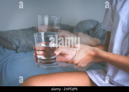 Femme tenant un verre d'eau dans des mains tremblantes et souffrant de symptômes de la maladie de Parkinson ou de tremblements essentiels. Banque D'Images