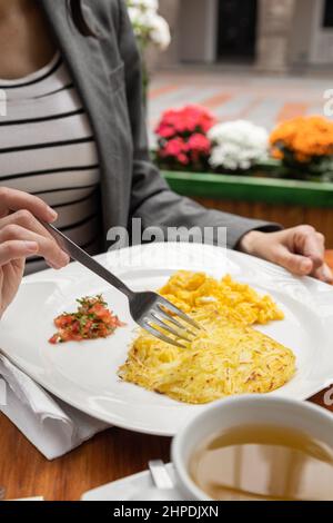 assiette servie avec un petit déjeuner frais, des œufs brouillés et une tasse de thé, détails des mains tenant une fourchette dans un restaurant, la nourriture et le style de vie Banque D'Images