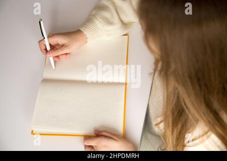 Apprentissage à distance, fille qui va écrire ou dessiner quelque chose sur un bloc-notes vierge sur le bureau, enfant droitier avec un stylo. L'enfant fait ses devoirs Banque D'Images