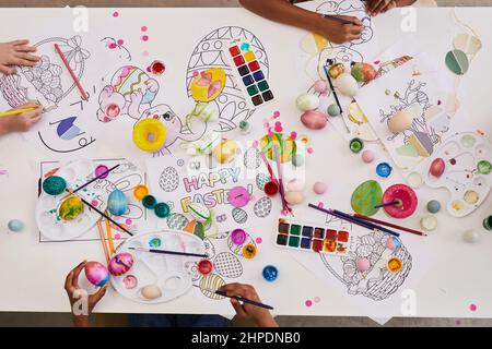 Image d'arrière-plan des enfants peignant des œufs de Pâques et des livres de coloriage sur table tout en appréciant l'art et la classe d'artisanat ensemble Banque D'Images