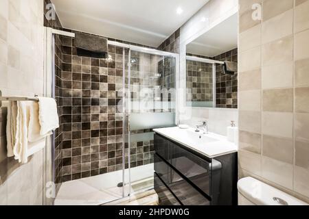 Salle de bains avec douche murale avec carrelage en marbre, miroir carré au mur et meuble noir avec évier en porcelaine blanche Banque D'Images