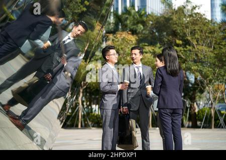 groupe de quatre jeunes hommes d'affaires asiatiques qui discutent à l'extérieur dans la rue Banque D'Images