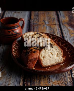 Une assiette mexicaine faite à la main, en argile ou boue, avec du pain doux et des raisins secs sur le dessus et une tasse de café ou de chocolat chaud cacao à l'arrière-plan. Banque D'Images