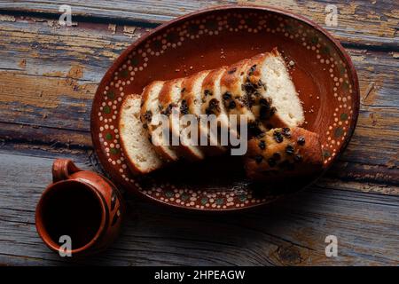 Une assiette mexicaine faite à la main, en argile ou boue, avec du pain doux et des raisins secs sur le dessus et une tasse de café ou de chocolat chaud cacao à l'arrière-plan. Banque D'Images